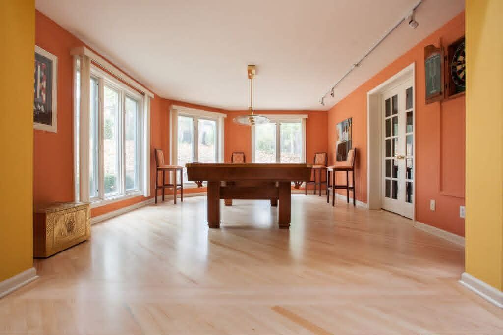 Empty sunlit room with light wood floors, coral walls, large windows, and a pool table in the center