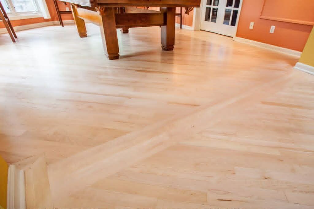 Light wood plank floor in an empty room with orange walls and a wooden table in the background