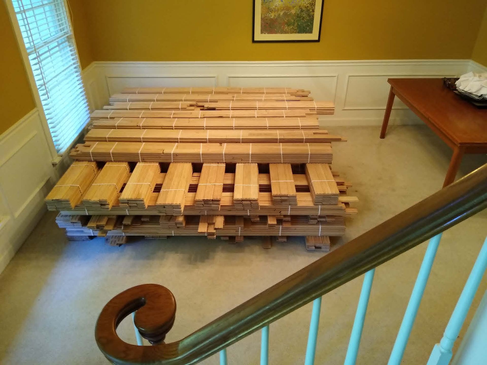 Stacked wooden pallets in a room with yellow walls, white wainscoting, and a table nearby