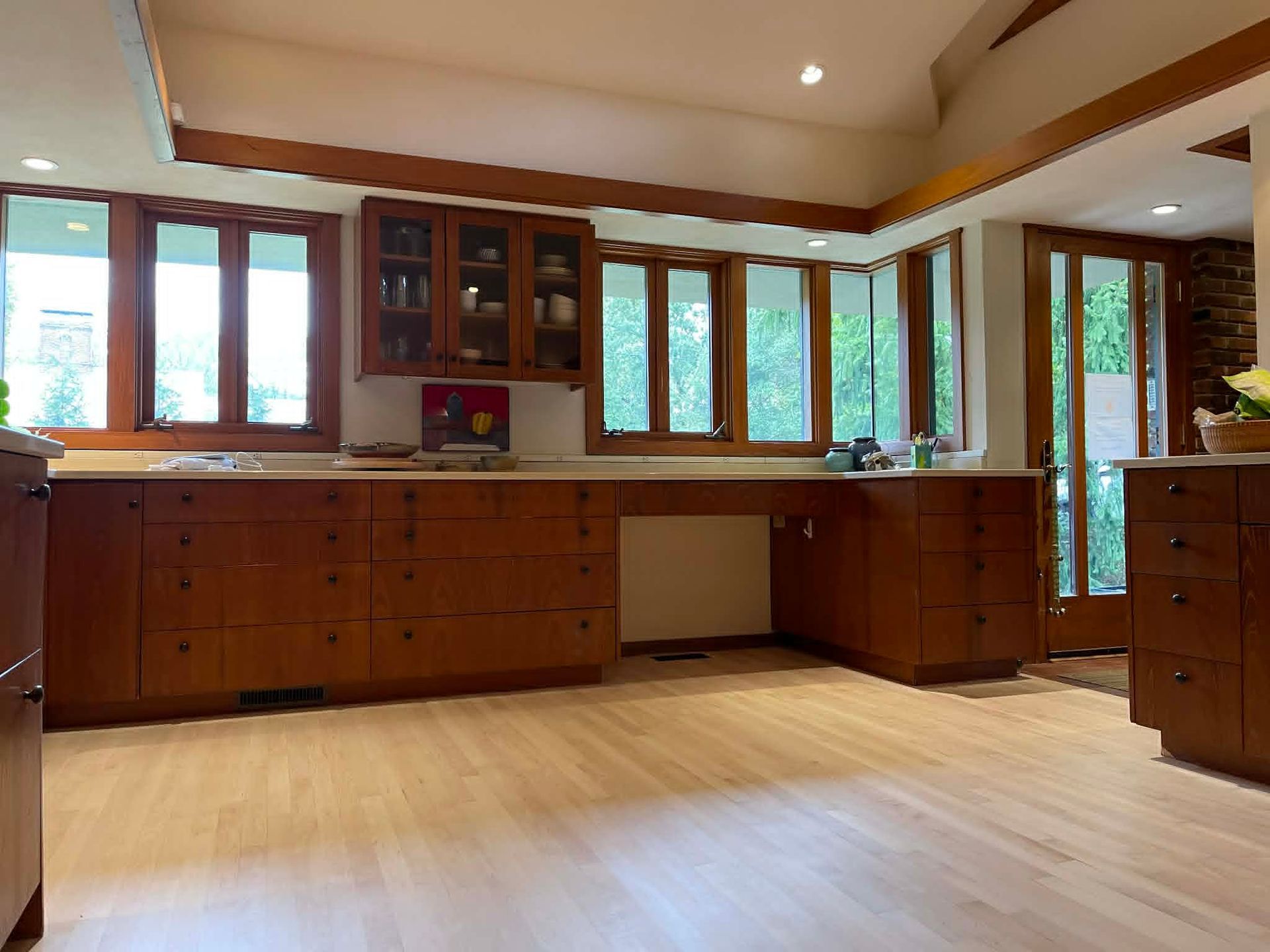 Modern kitchen with wooden cabinets, large windows, and light wood flooring