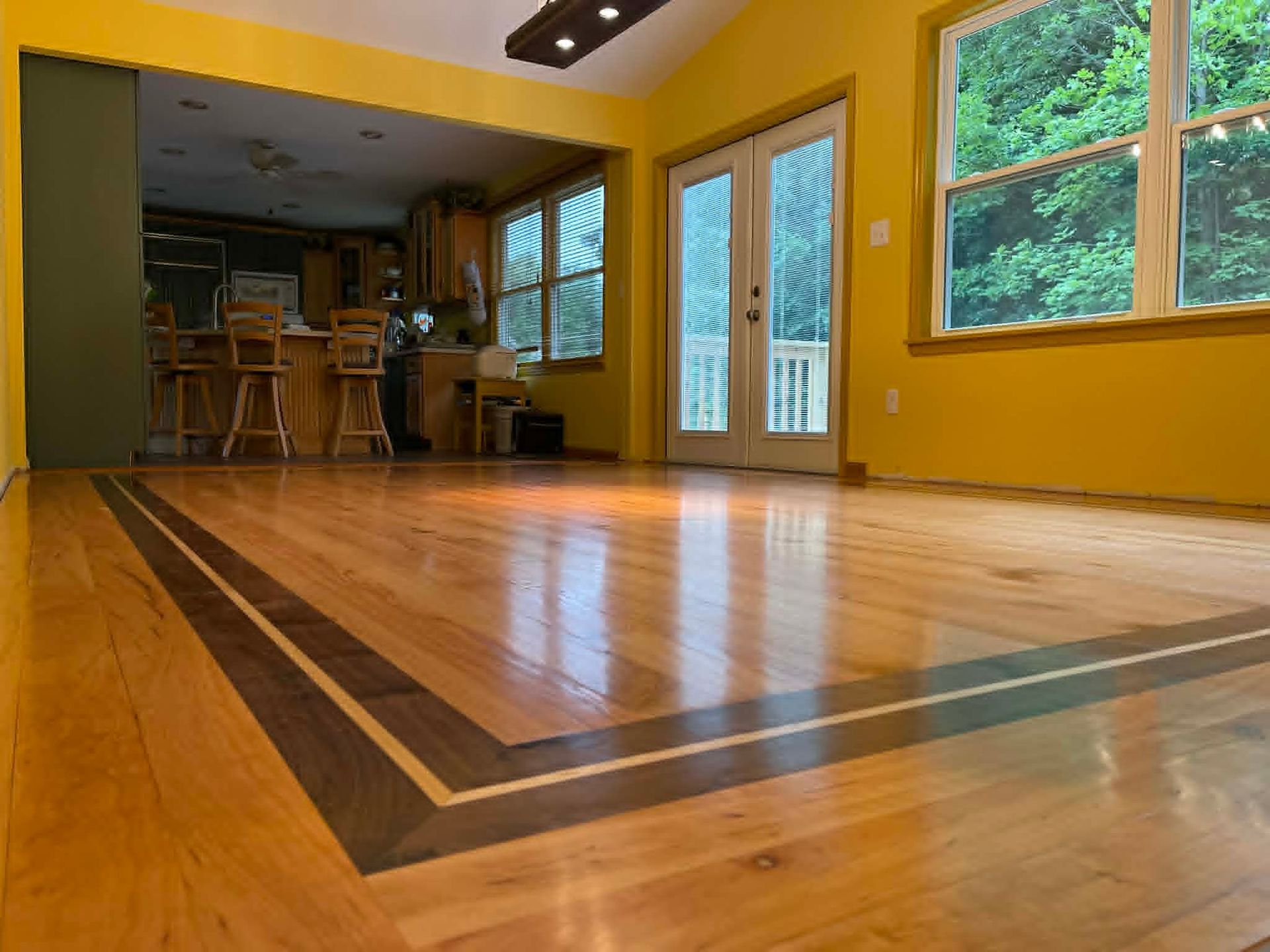 Empty living room with polished wooden floor, yellow walls, and large windows and glass doors.