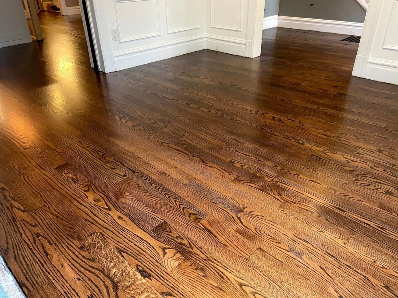 A view of dark, polished hardwood flooring in a room with white wainscoting and trim.