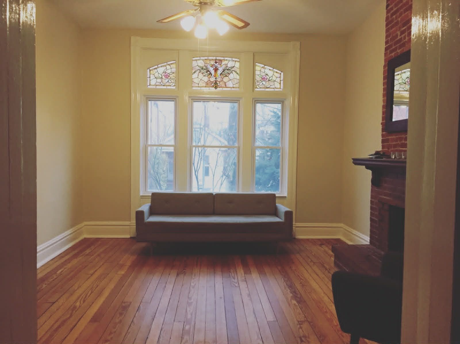 Empty sunlit room with hardwood floors, a large window, and a bench beneath it.