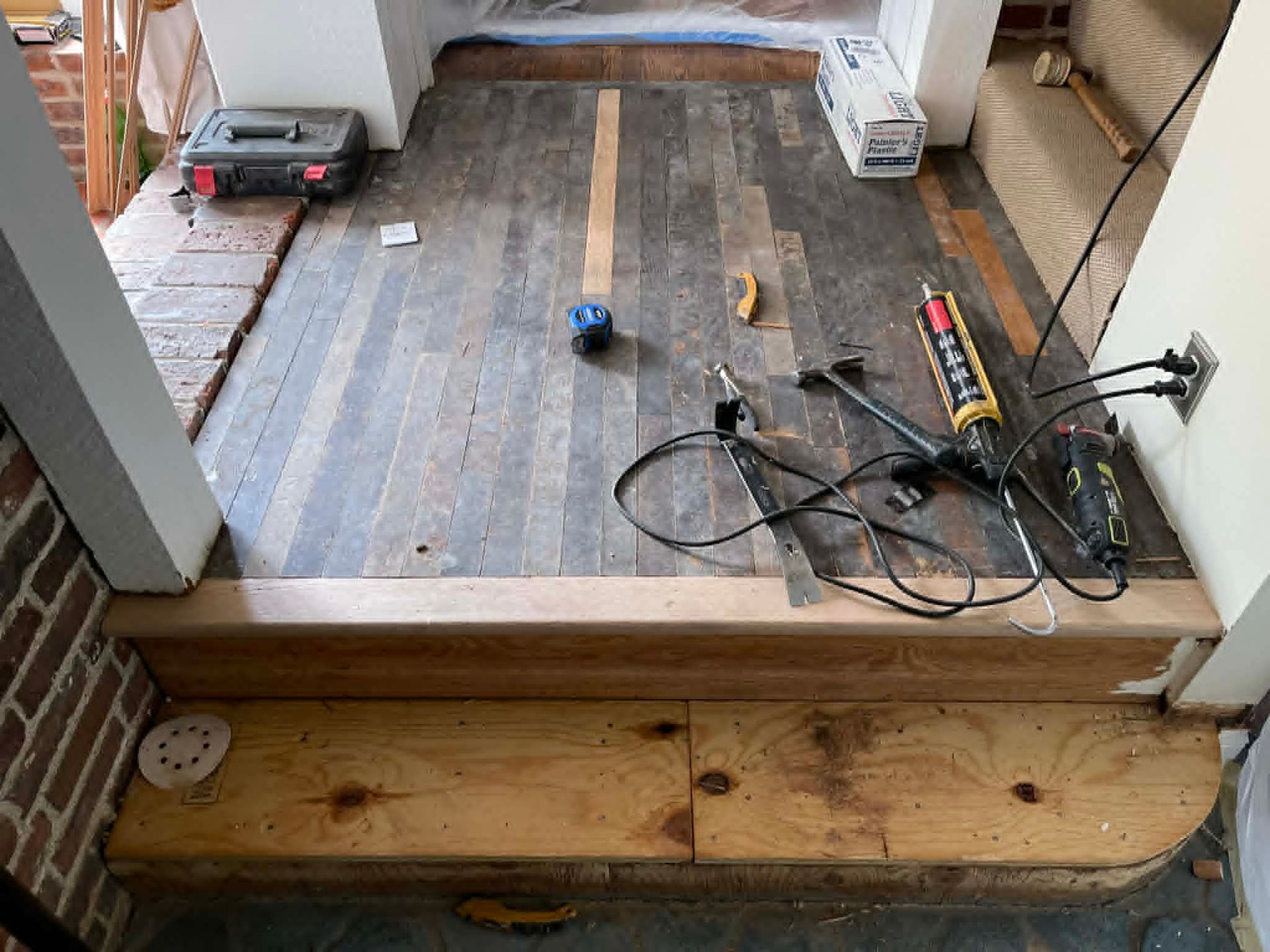 Messy doorway with tools, cables, and flooring materials on a partially finished floor