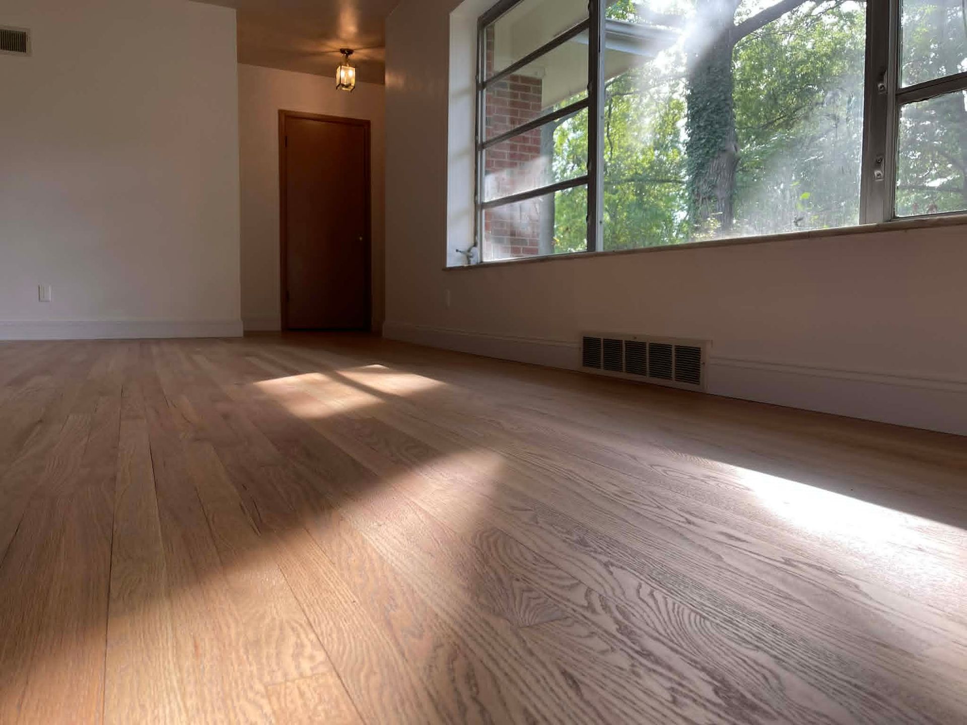 Empty sunlit room with hardwood floor, large windows, and an open door