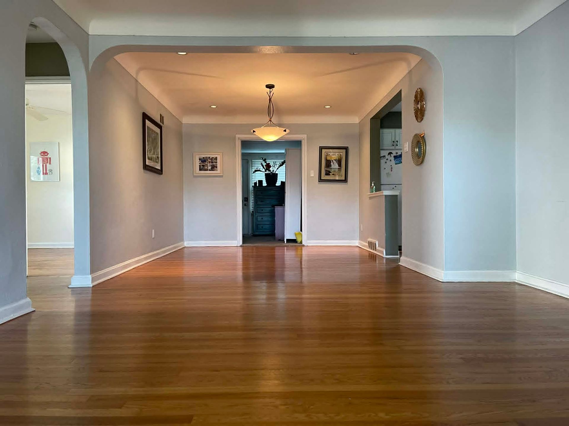 Empty hardwood-floored living room with light blue walls and arched doorway to a hallway