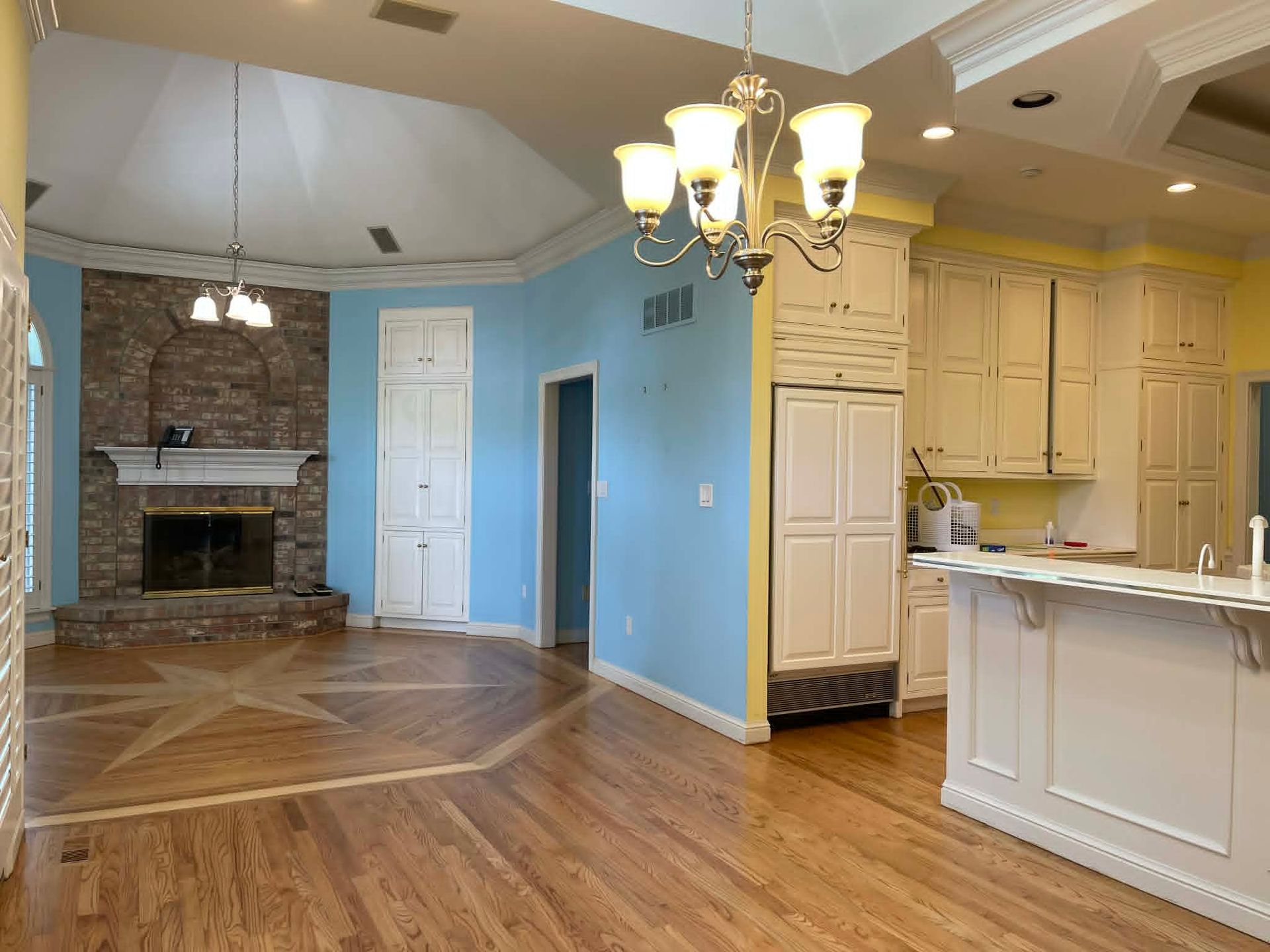 Empty open-plan kitchen and living room with hardwood floors, blue walls, and a stone fireplace.