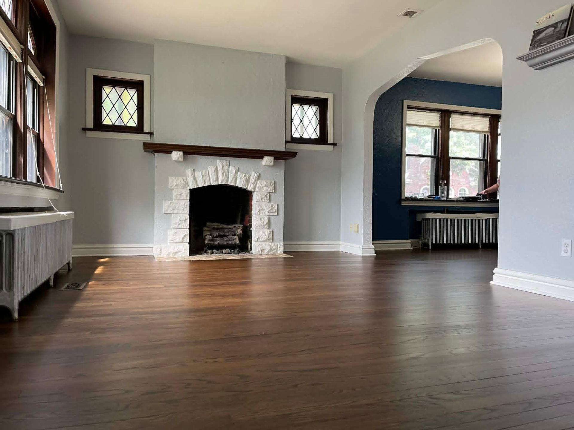 Empty living room with wood floors, stone fireplace, and two small stained-glass windows