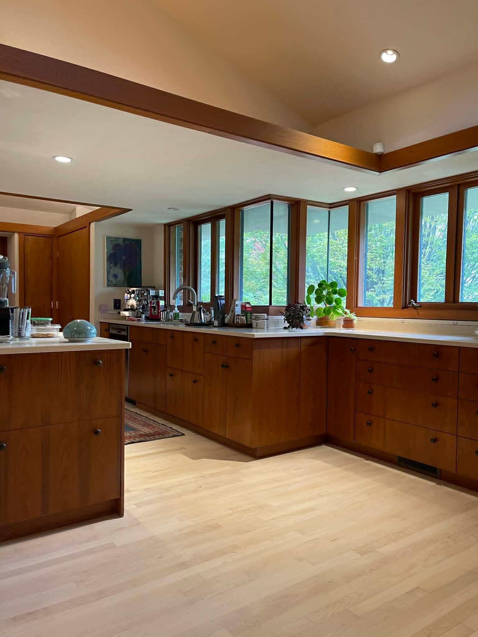 Spacious modern kitchen with wooden cabinets, light floors, and large windows overlooking greenery