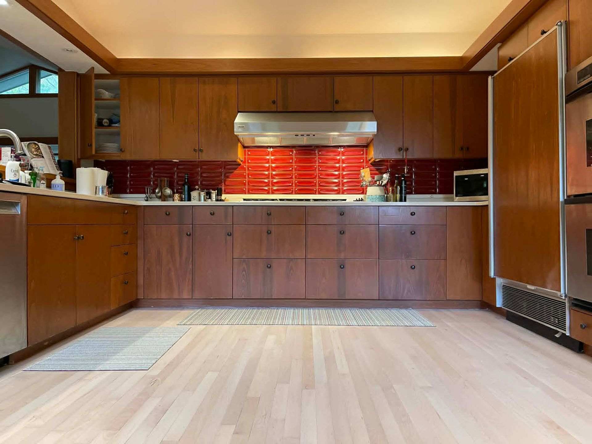 Empty modern kitchen with wood cabinets, red tile backsplash, and light hardwood floor