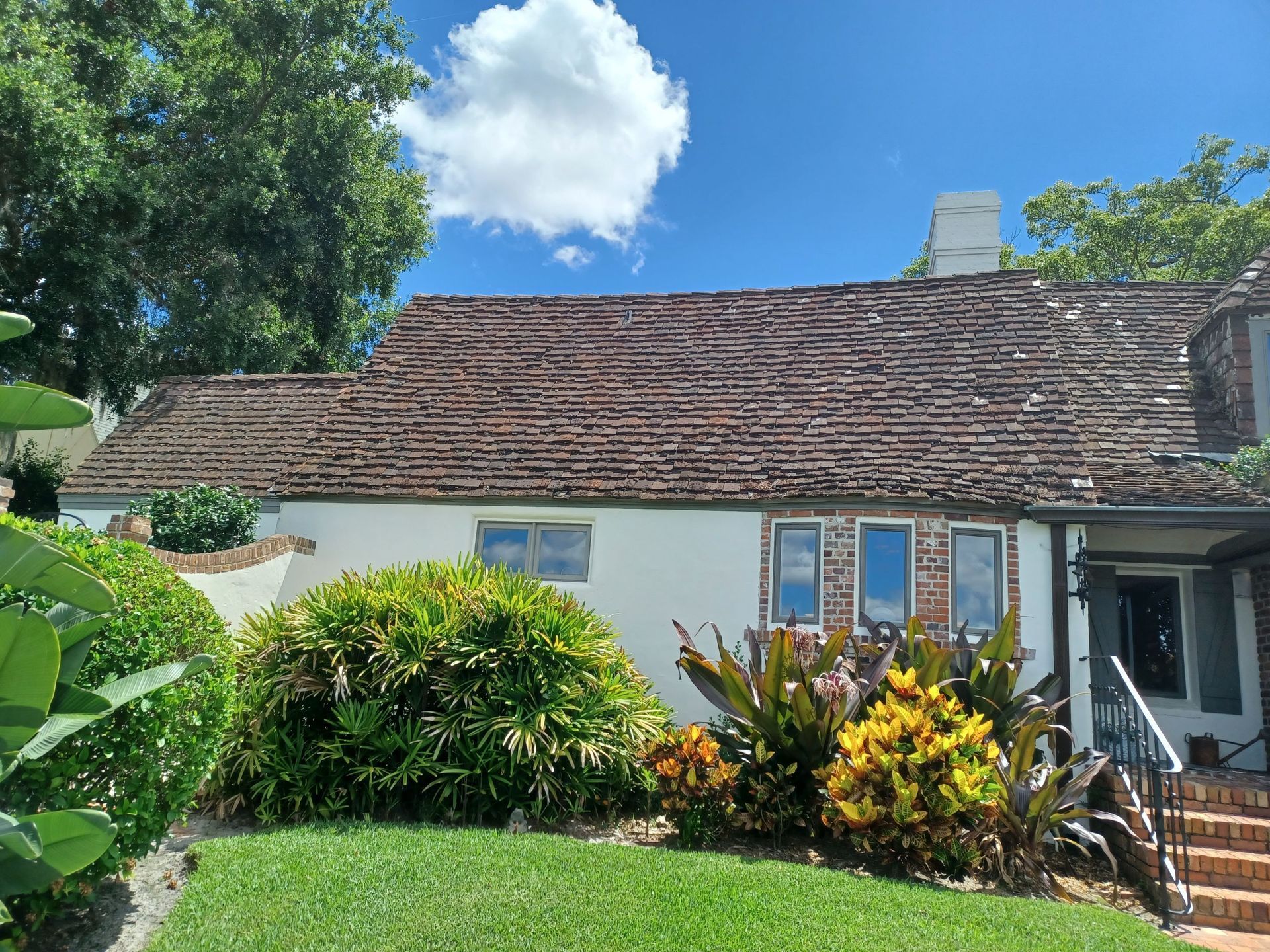 A white house with a brick roof and a lush green yard