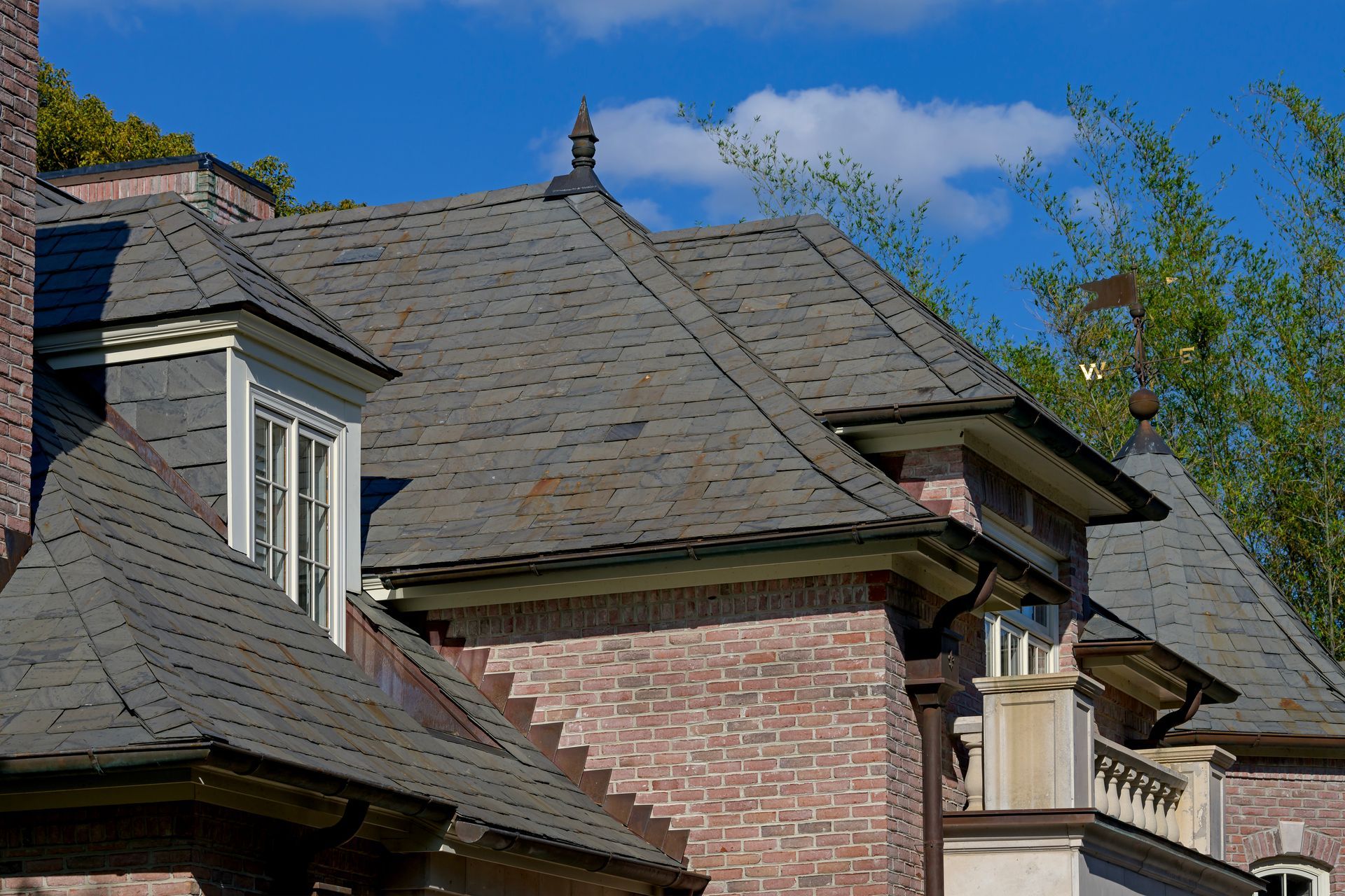 A brick house with a gray roof and a weather vane on top of it.