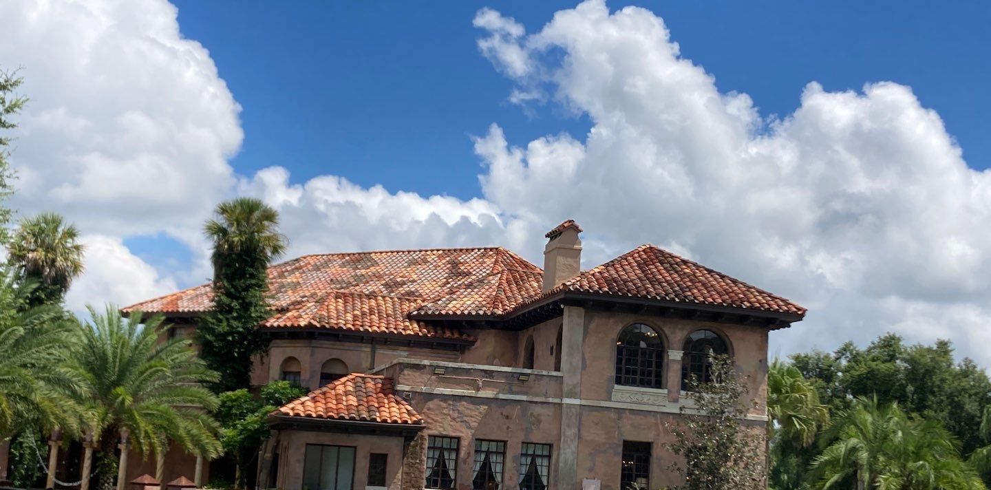 A large house with a tiled roof is surrounded by palm trees on a sunny day.