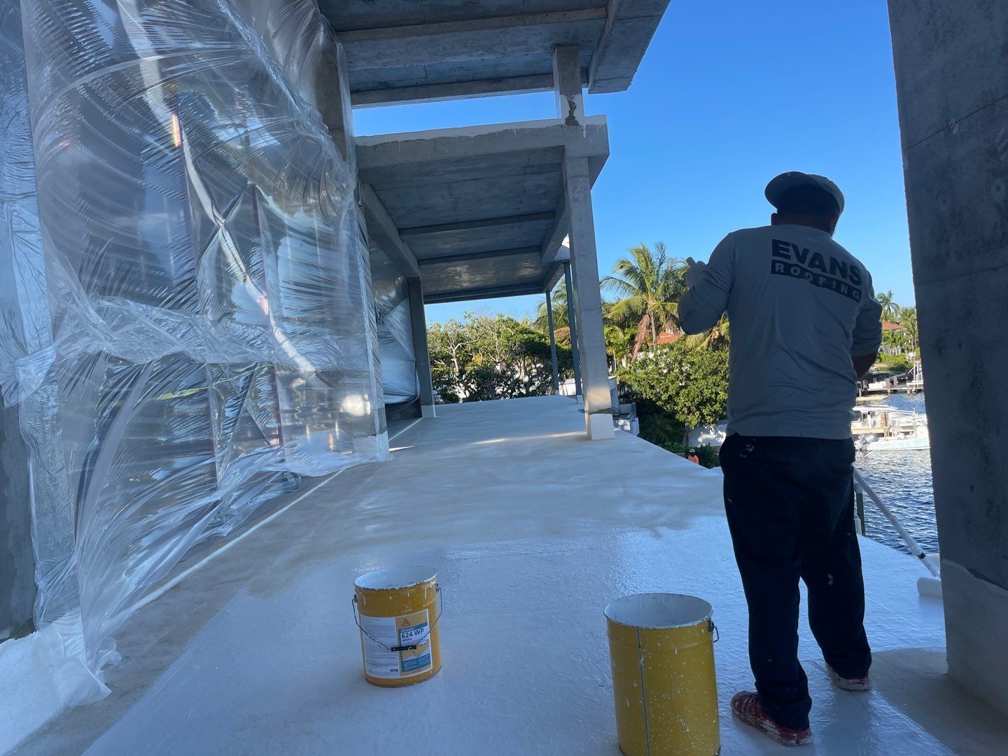 A man is painting a roof with a bucket of paint.