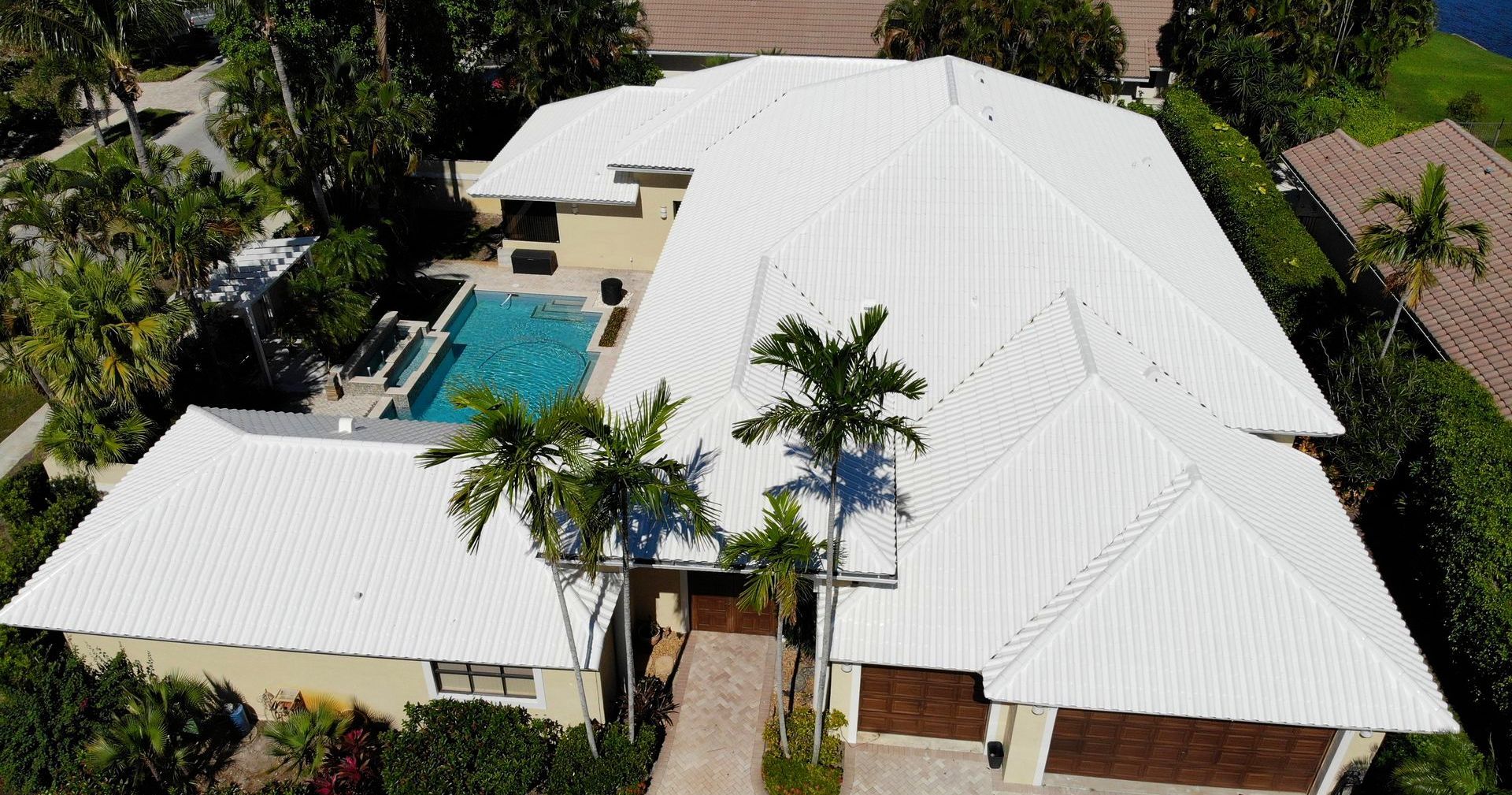 An aerial view of a large house with a white roof and a pool.