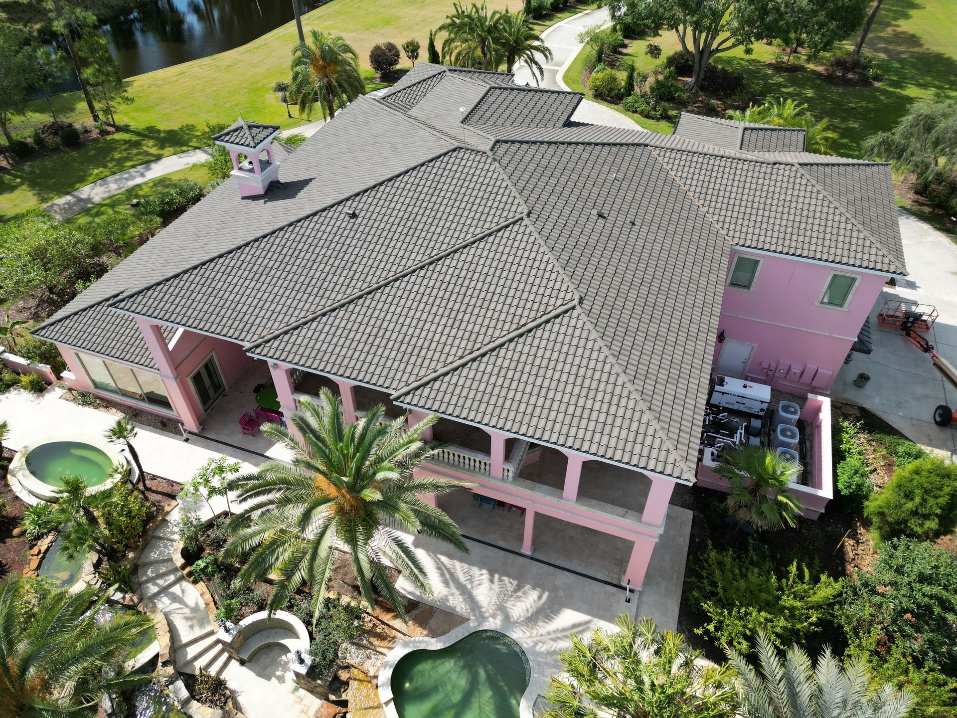 An aerial view of a large pink house with a gray roof surrounded by palm trees.