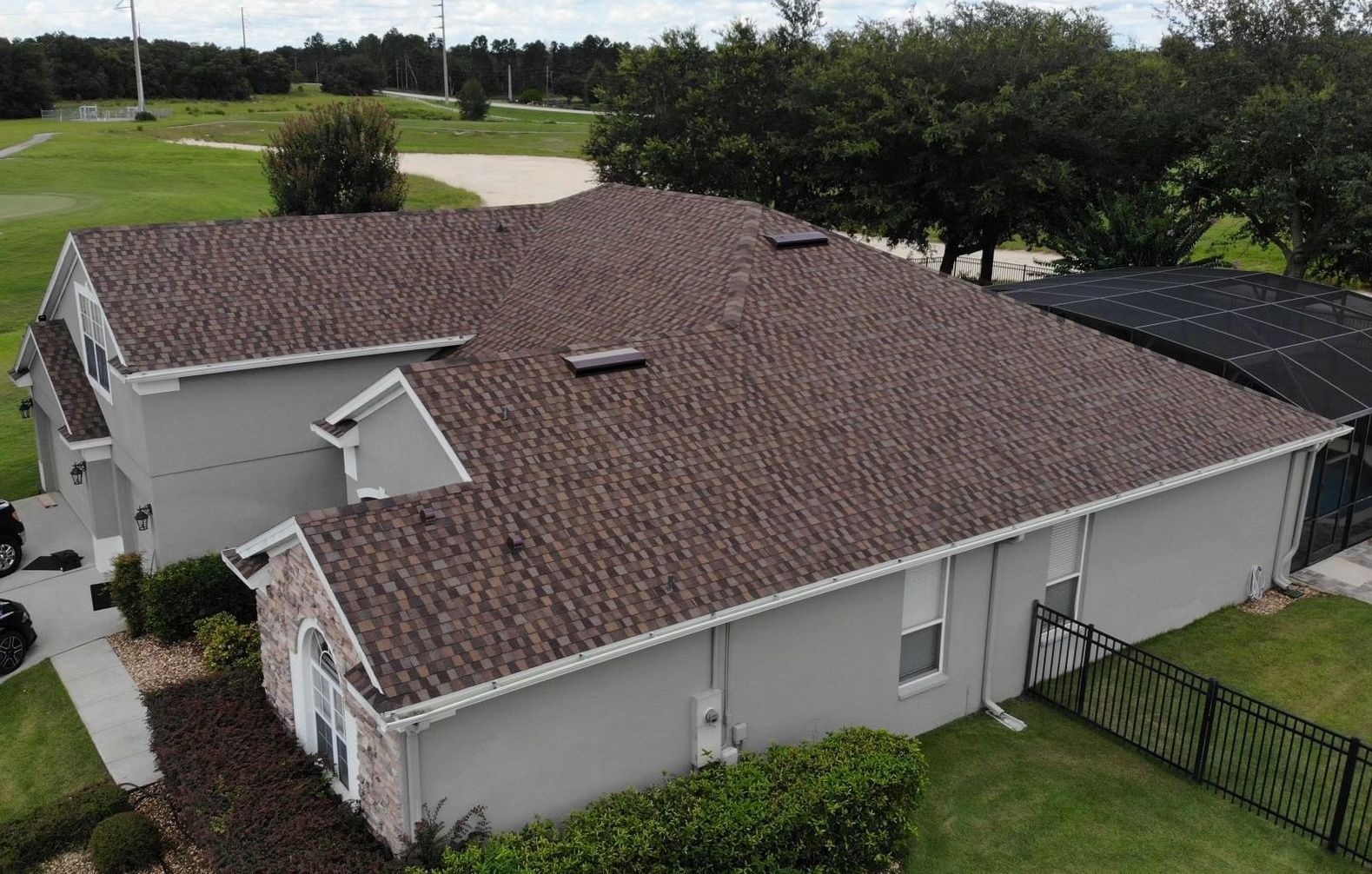 An aerial view of a house with a new roof and a golf course in the background.