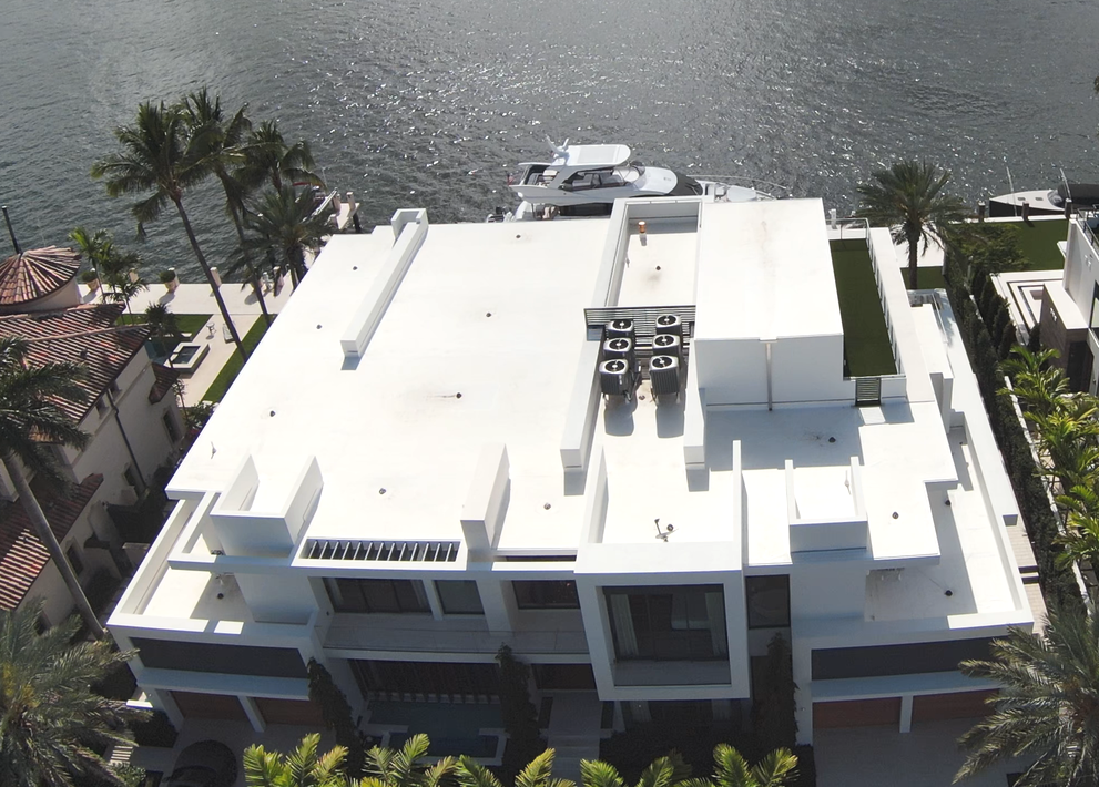 An aerial view of a large white house with a boat in the background