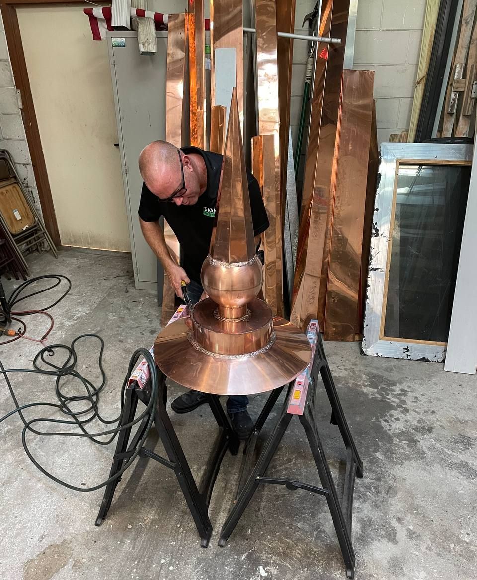 A man is working on a copper object in a garage.
