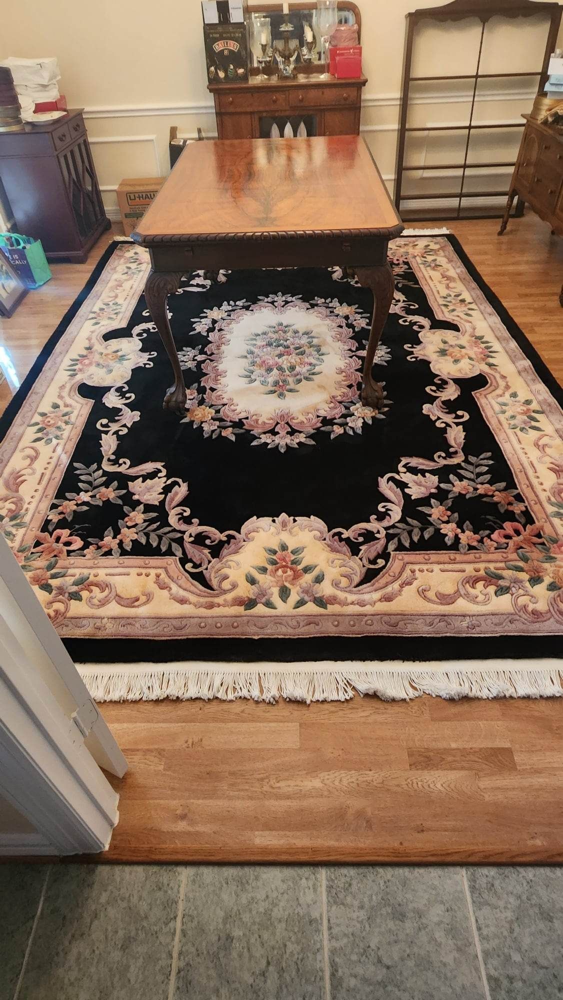 Black rug with floral design under a dining table in a room with hardwood floor and antique furniture.