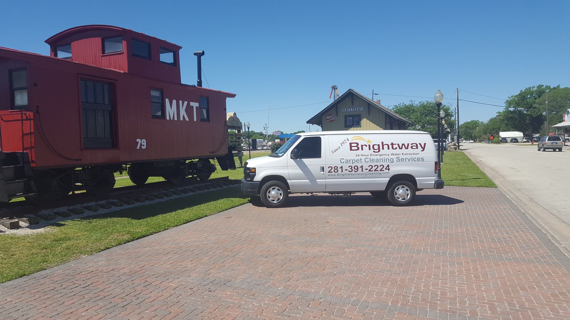 White van with BrightWave logo parked near a red train caboose and a brick street. Sunny day.