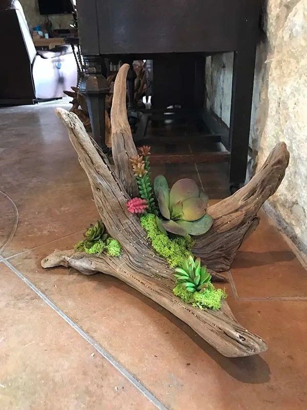 A piece of driftwood with flowers in it is sitting on a tiled floor.