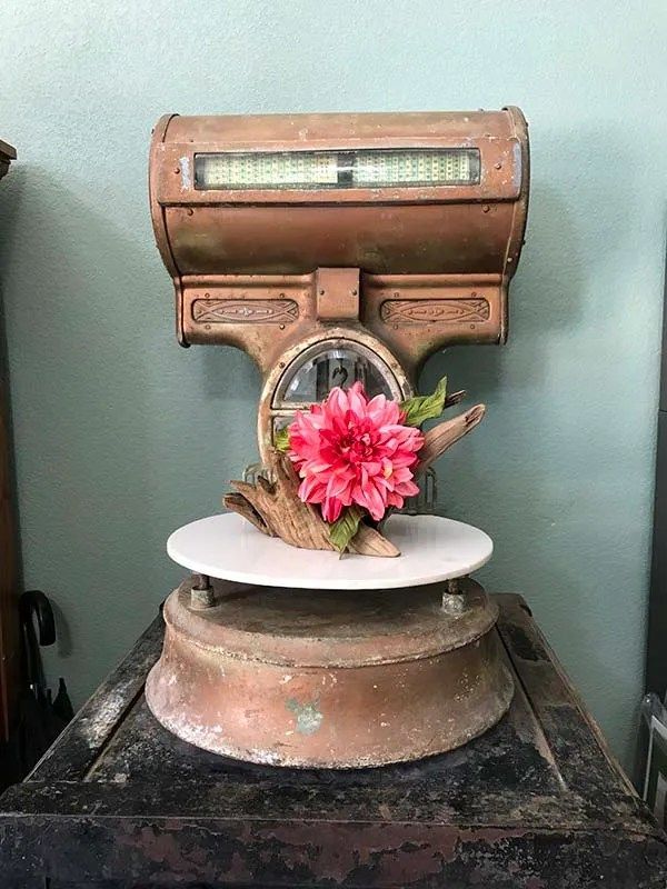 An old scale with a pink flower on top of it.