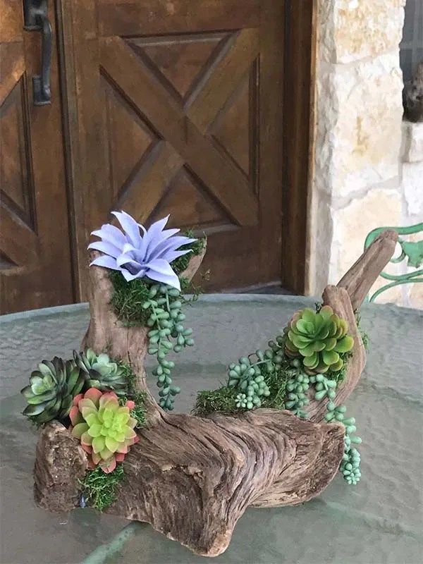 A piece of wood with flowers and succulents on it is sitting on a table.