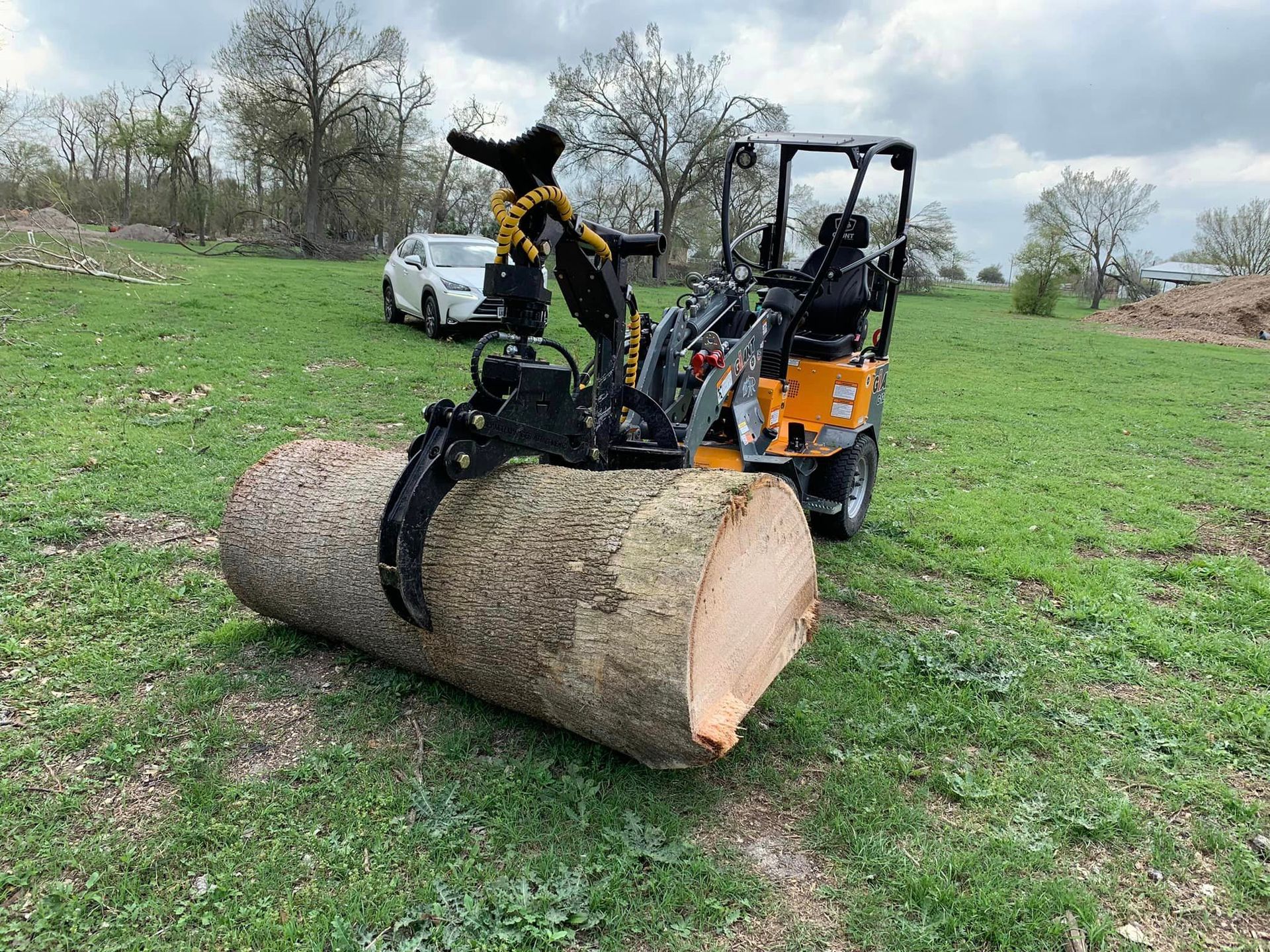 A tractor is carrying a large log in a field.
