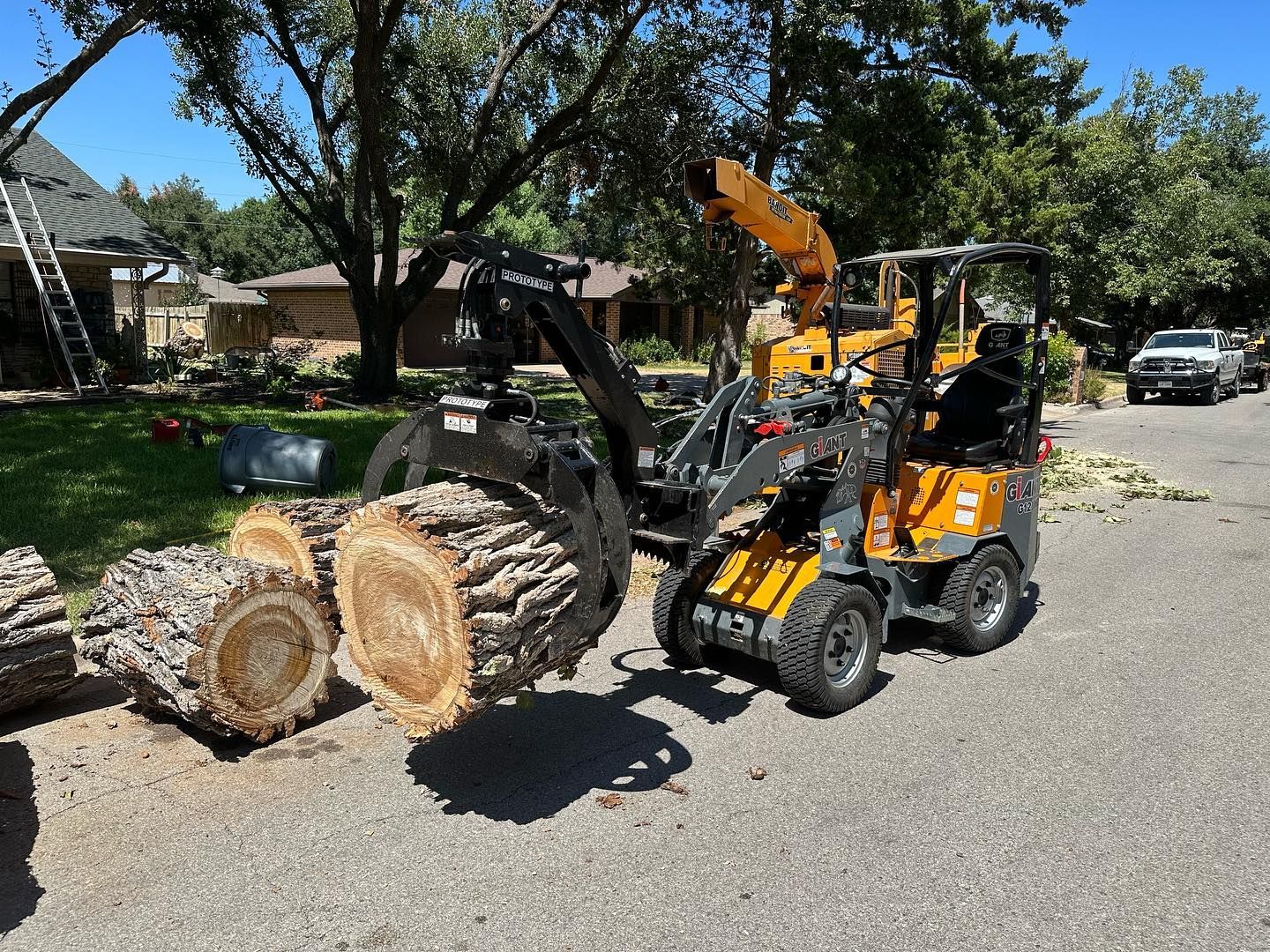 A tractor is carrying a pile of logs down a street.