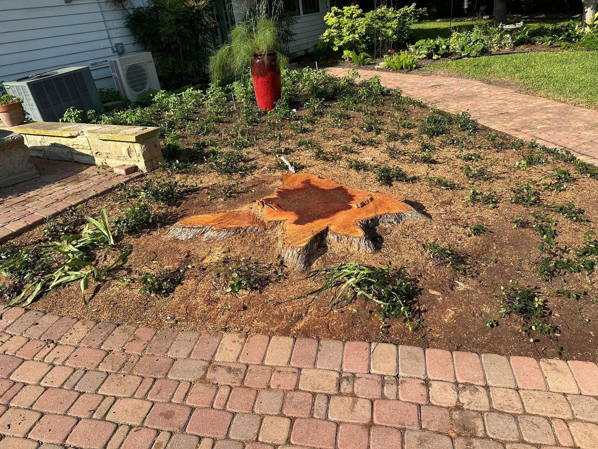 A tree stump in the middle of a brick driveway.