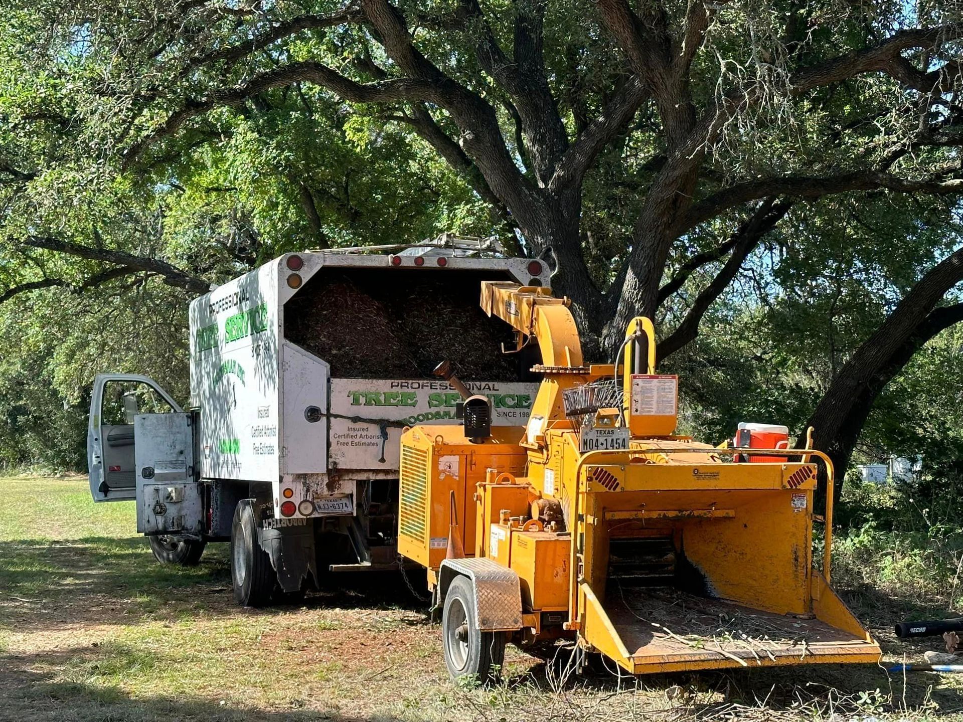 A tree chipper is sitting next to a truck in a field.