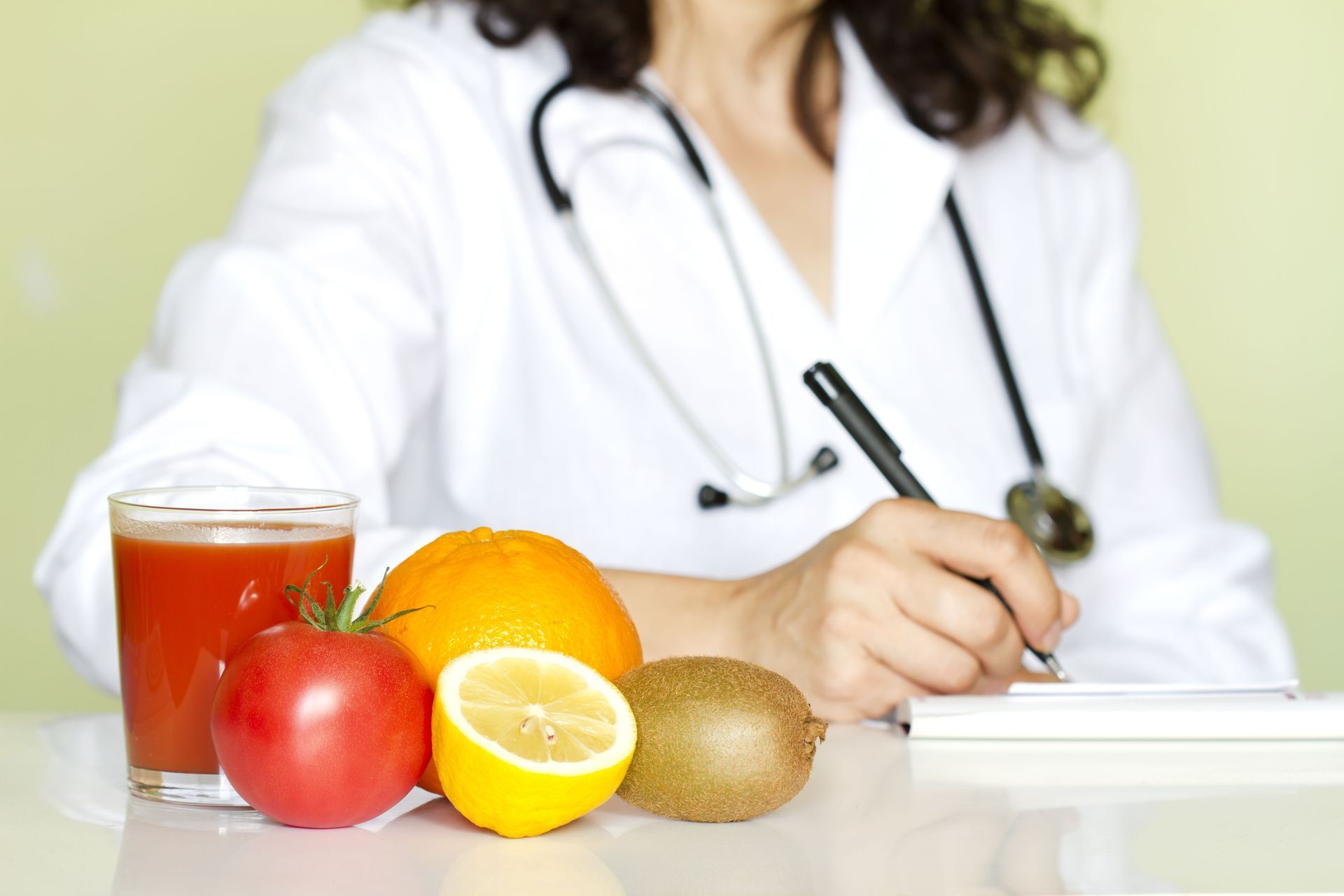 Doctor with stethoscope writing, fruit, juice on desk.