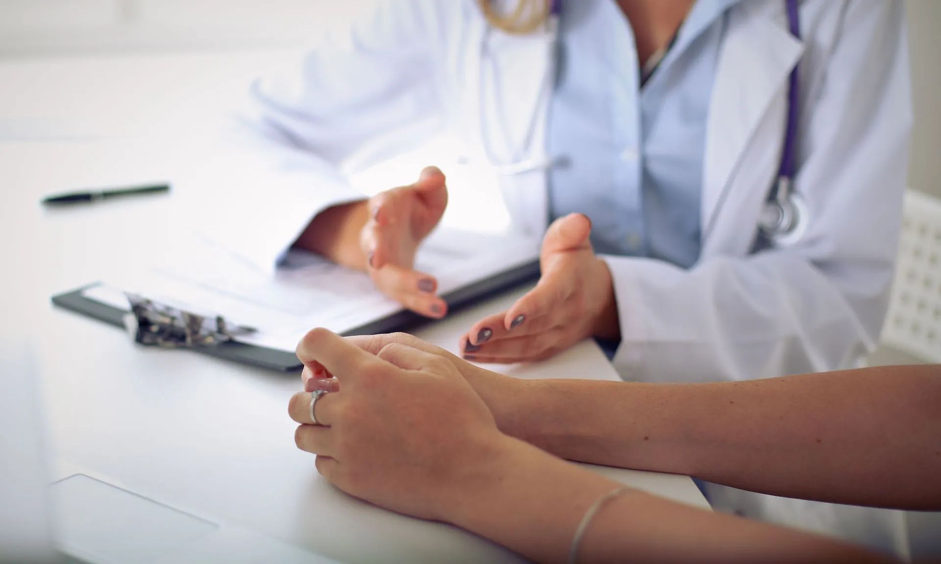 Doctor gesturing while speaking to a patient, seated at a desk.