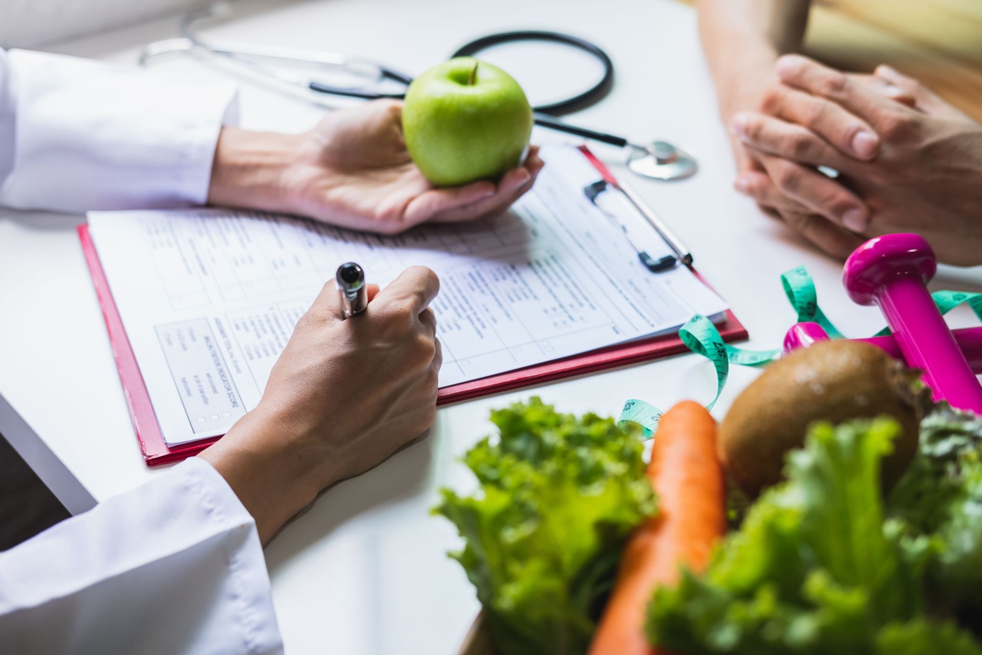 A dietitian holding an apple, writing on a clipboard with fruits and vegetables nearby.