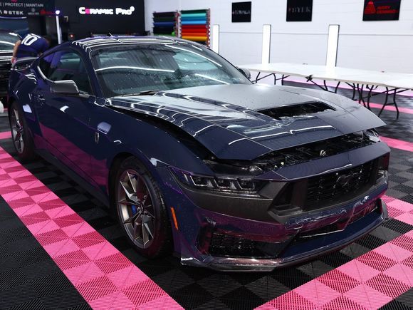 Blue Ford Mustang with damaged front in a garage setting with colorful material samples.