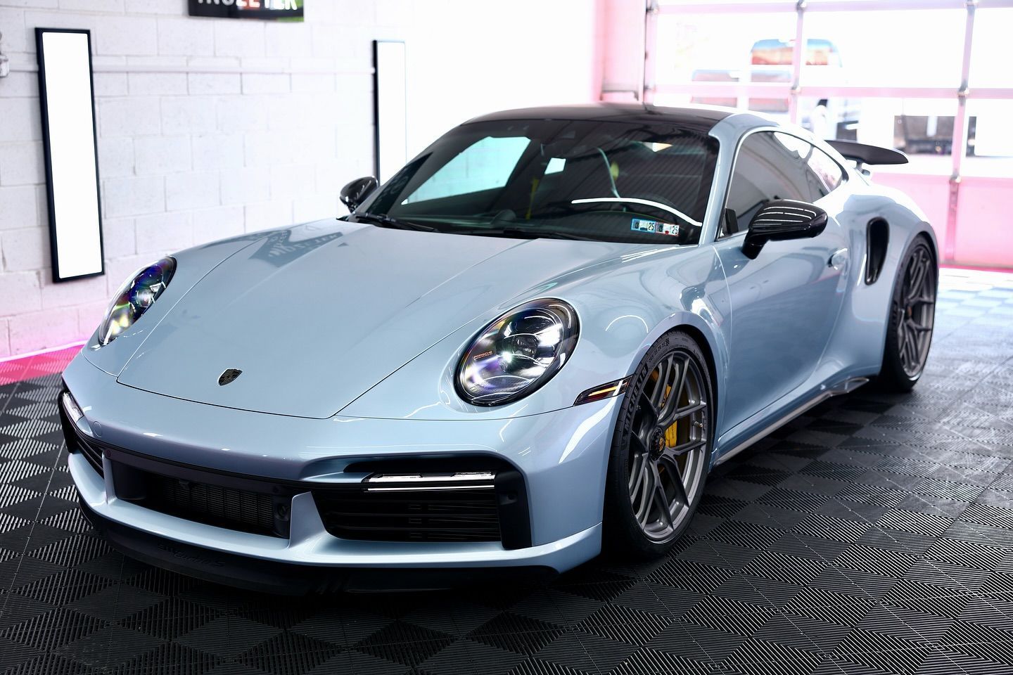 Light blue Porsche 911 Turbo S parked in a garage, black roof, yellow brake calipers, dark wheels.
