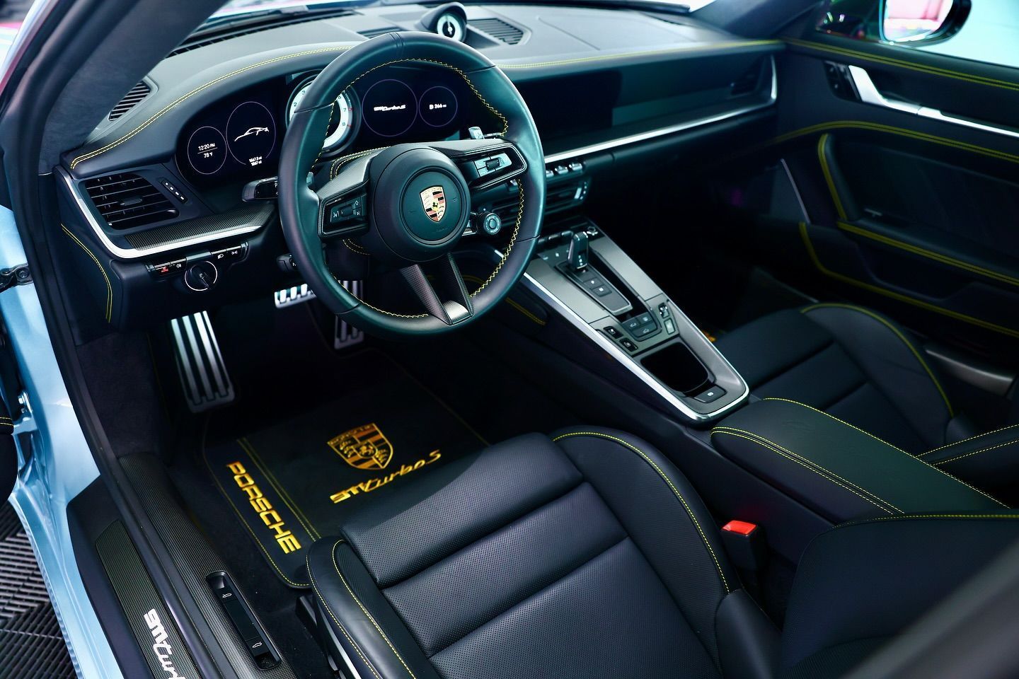 Black leather Porsche 911 Turbo S interior with yellow stitching, floor mats, and steering wheel.