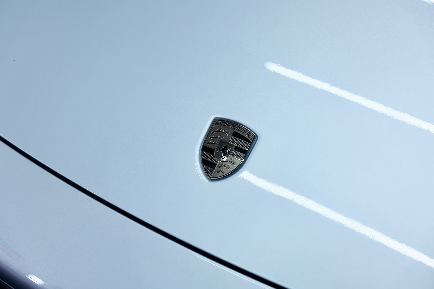 Porsche emblem on a light blue car hood, reflecting bright lights.