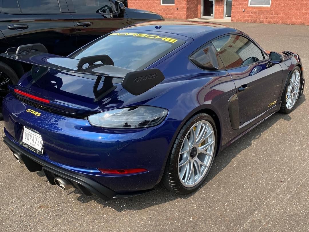 Blue Porsche sports car with a large rear wing parked on pavement.