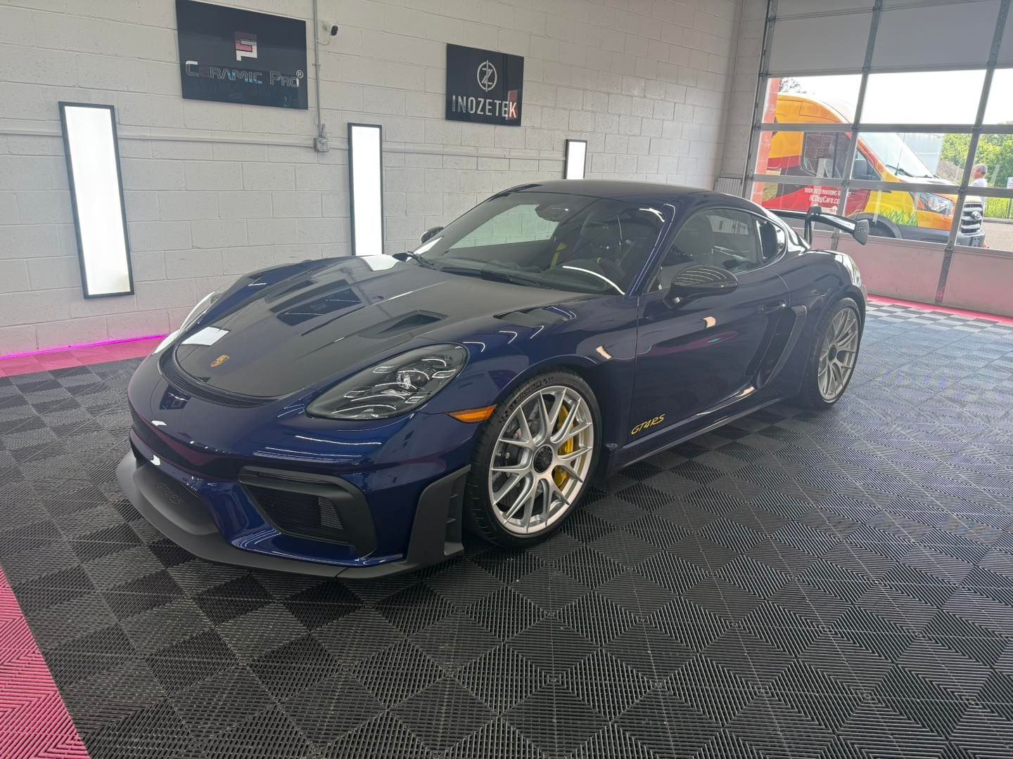 Blue Porsche sports car parked inside a garage with black flooring and white lighting.