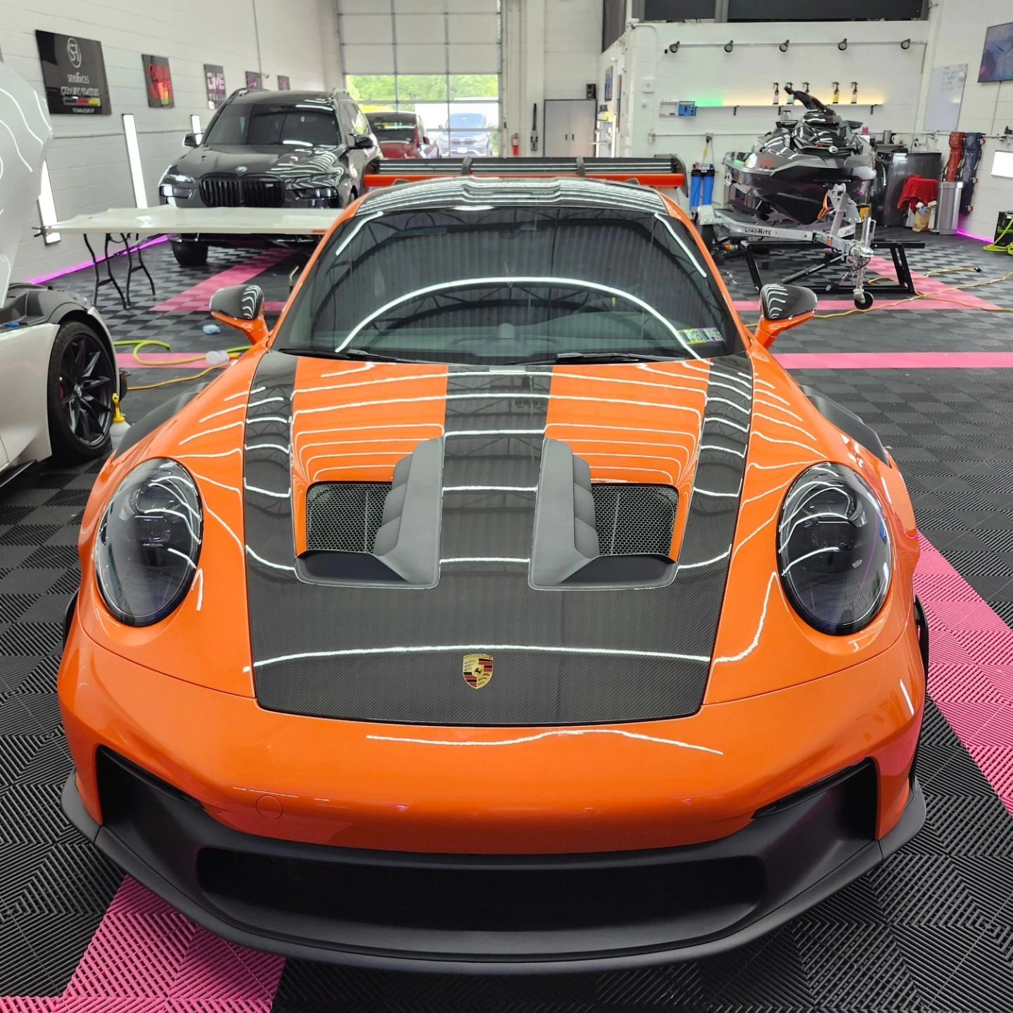 Bright orange Porsche 911 GT3 RS with carbon fiber hood in a garage.