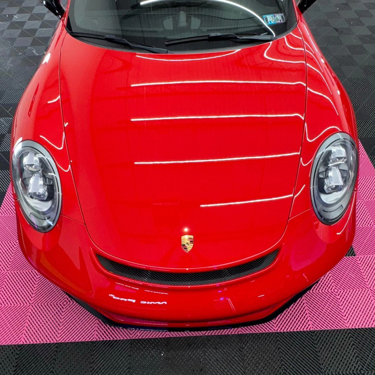 Red Porsche sports car, front view, shiny finish, on a pink tiled floor.