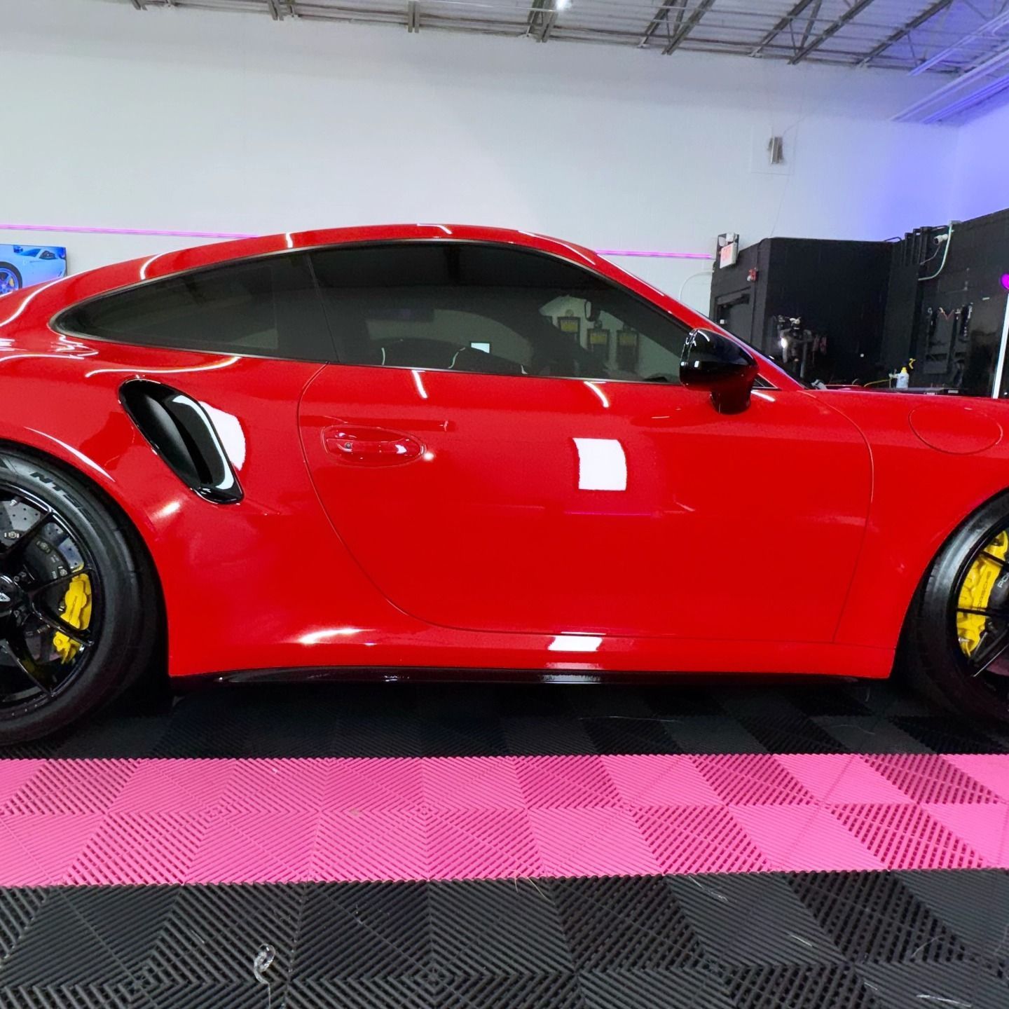 Red Porsche with black wheels and yellow calipers, parked indoors on a pink and black tiled floor.