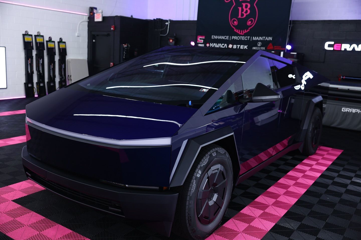 Dark blue Tesla Cybertruck parked on pink and black checkered floor indoors.
