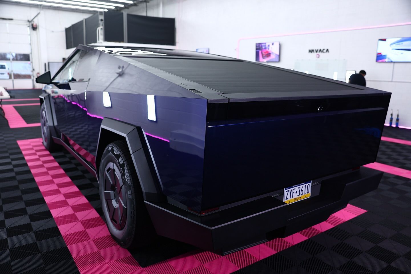 Rear view of a dark blue Tesla Cybertruck with a covered bed, parked on a pink and black checkered floor.