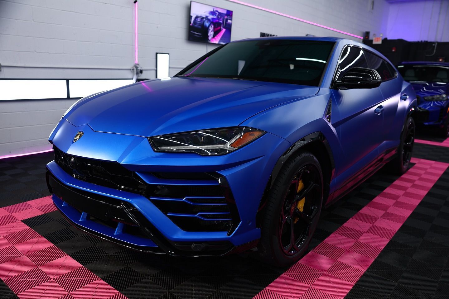 Blue Lamborghini Urus SUV in a garage with pink neon lighting.