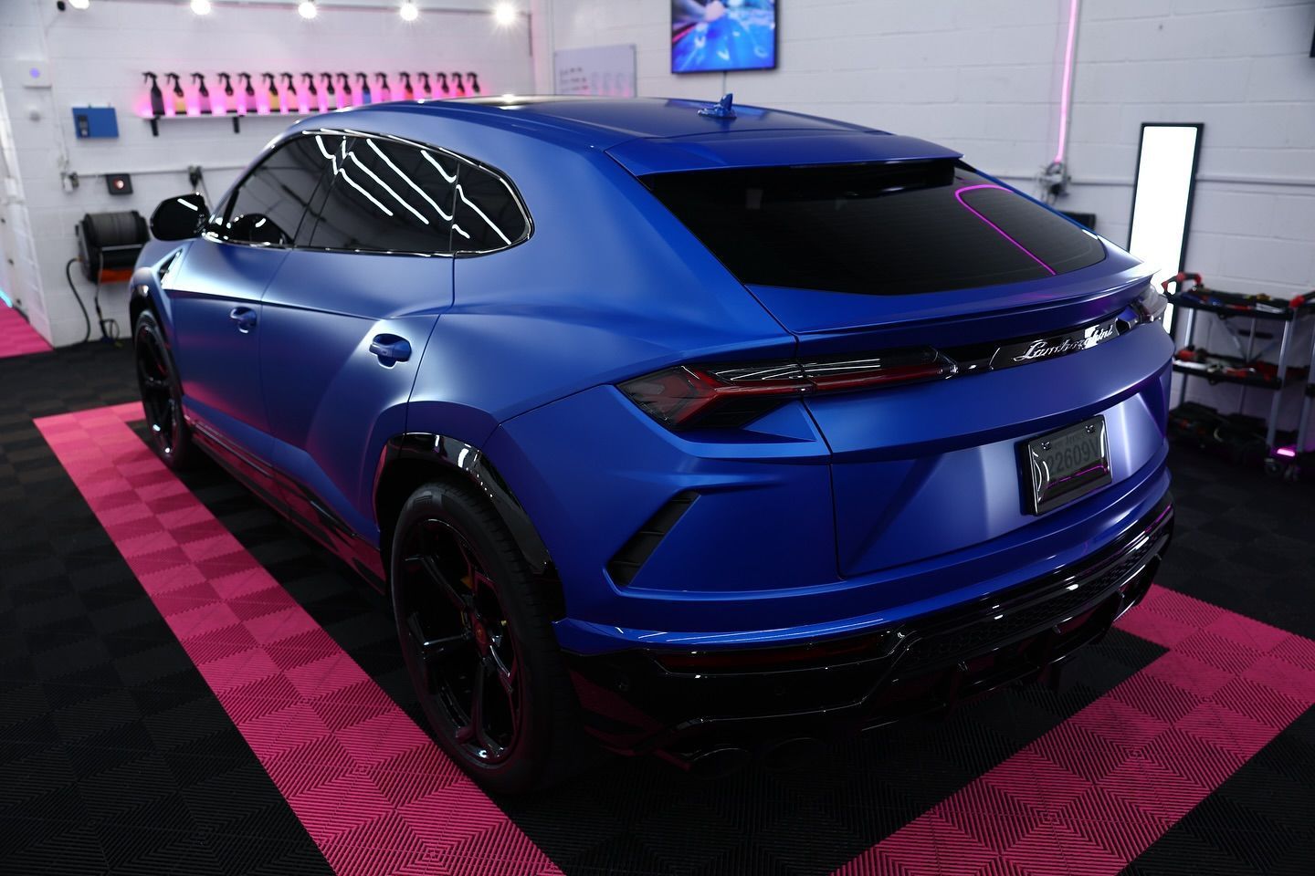 Blue Lamborghini Urus SUV in a garage with pink flooring.
