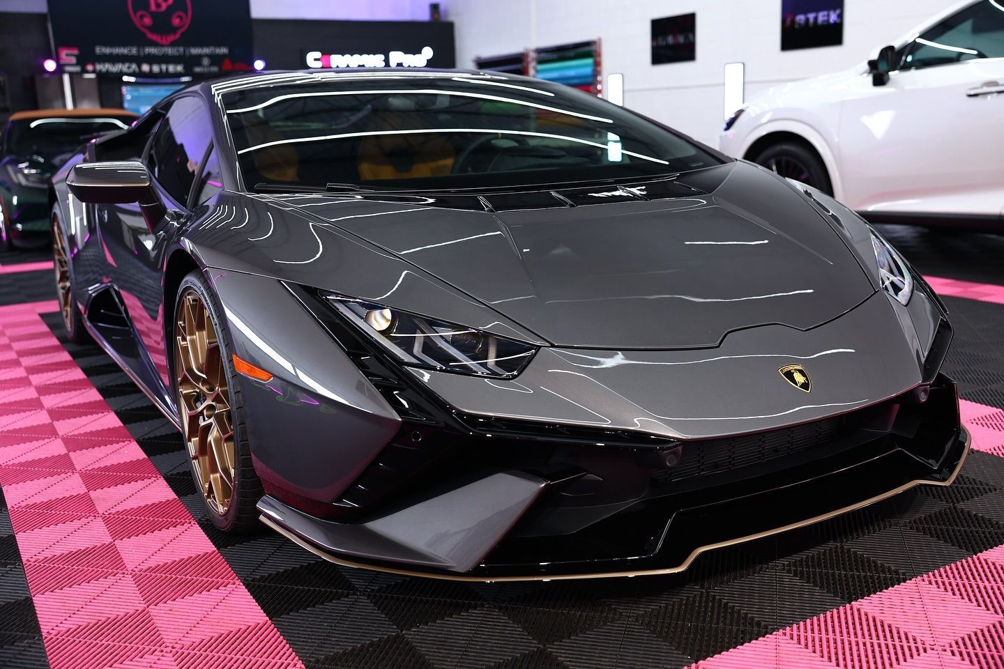 Gray Lamborghini sports car with gold wheels, displayed indoors on pink-tiled flooring.