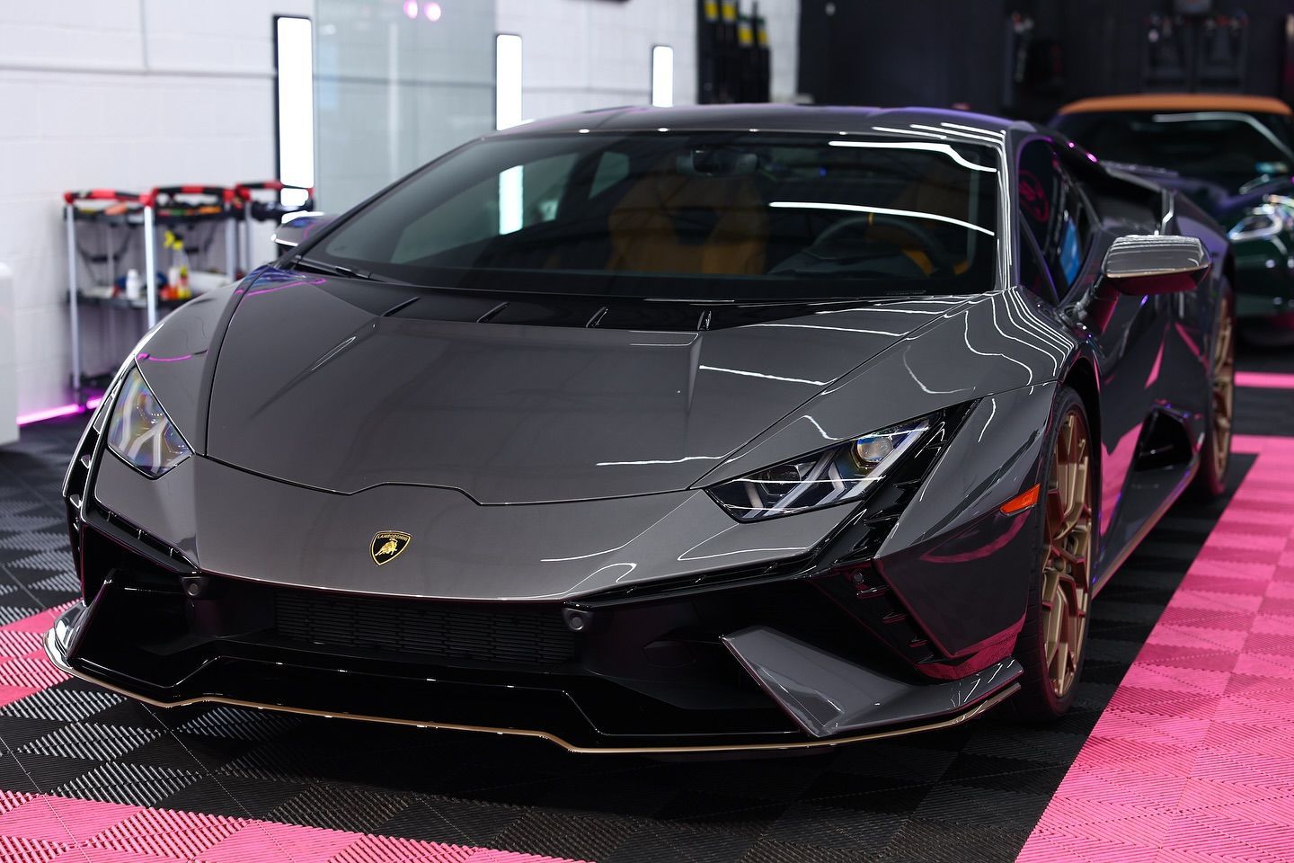 Gray Lamborghini Huracan with gold accents, parked indoors on a pink-tiled floor.